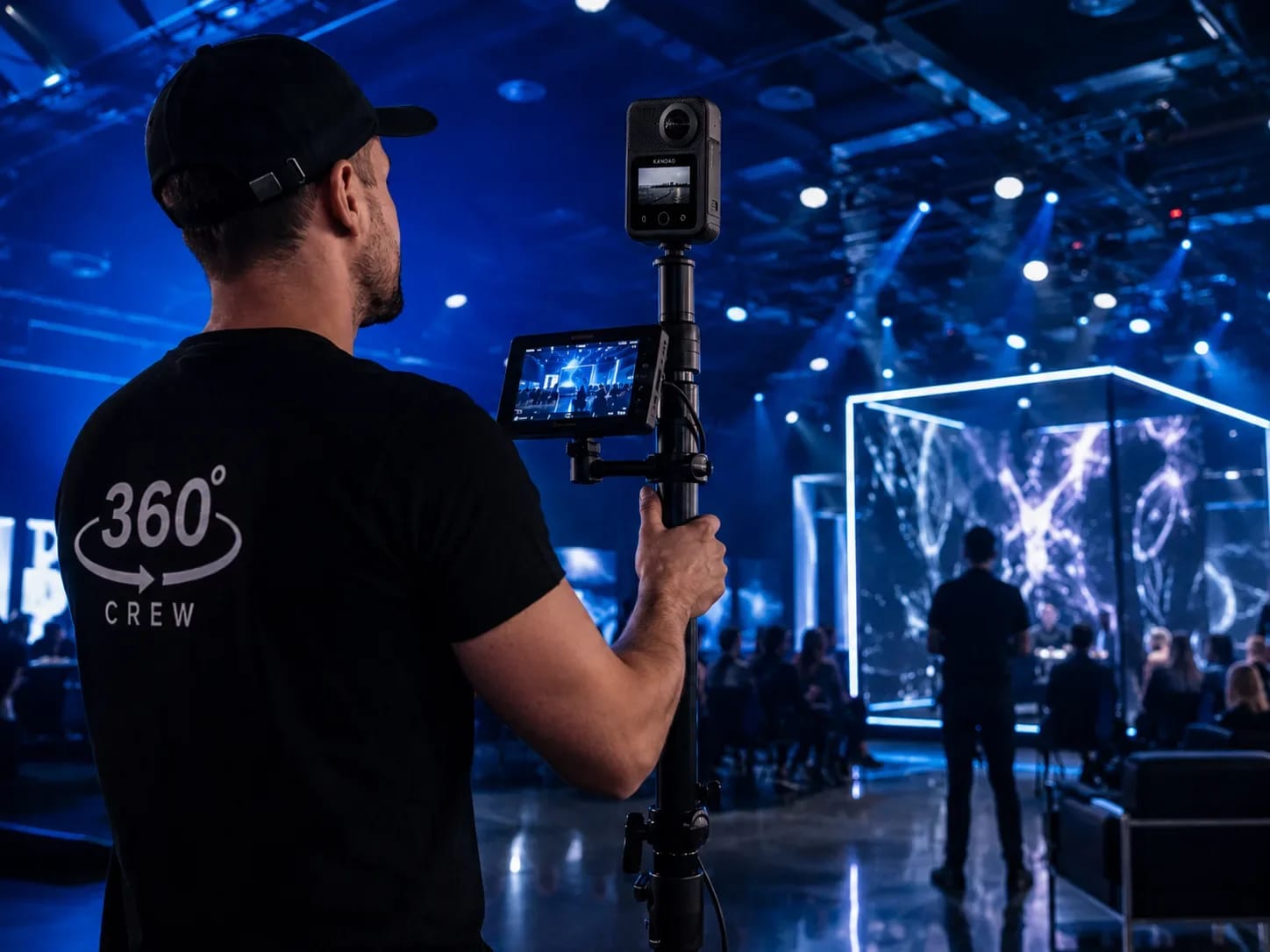 Opérateur en t-shirt 360° Crew filmant avec une caméra 360° sur perche un spectacle scénique sous éclairages bleus